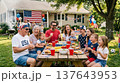 Group of people celebrating at outdoor picnic table decorated with American flag and summer banners. Summer celebration, picnic, holiday, patriotic, USA. 137643953