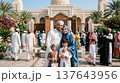 Family in traditional dress standing near mosque on sunny day during holiday celebration. Holiday, mosque, tradition, family, Middle East. 137643956