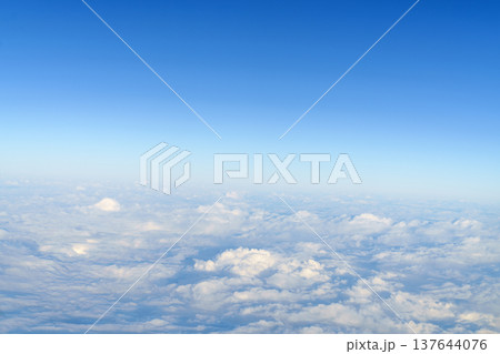 Wide aerial shot of soft white fluffy clouds under a clear bright blue sky during daytime. Breathtaking high altitude view from an airplane window. Peaceful atmospheric nature background. Wide aerial shot of soft white fluffy clouds under a clear bright blue sky during daytime. Breathtaking high altitude view from an airplane window. Peaceful atmospheric nature background. 137644076