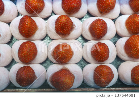 Top-down view of fresh strawberry mochi or ichigo daifuku arranged in neat rows. Each soft pink rice cake is topped with a whole red berry. Authentic Japanese wagashi dessert and sweet snack. 137644081