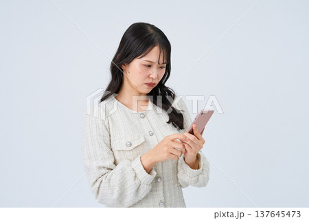 困った表情でスマートフォンの画面を見る若い女性 困った表情でスマートフォンの画面を見る若い女性 137645473