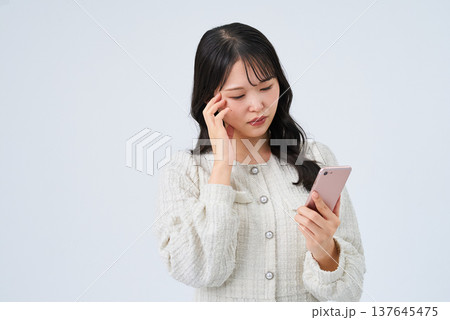 困った表情でスマートフォンの画面を見る若い女性 困った表情でスマートフォンの画面を見る若い女性 137645475