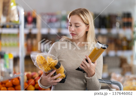 Female shopper chooses between spaghetti and pasta while shopping at supermarket 137646002
