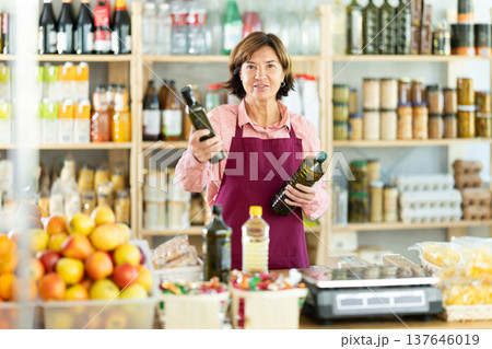 Experienced female salesperson offers choice of buying bottle of vegetable oil or olive oil in grocery store 137646019