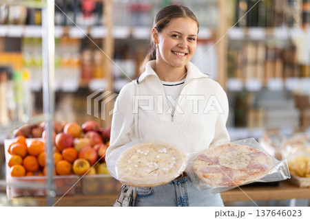Female buyer carefully reads labels on frozen pizza - she chooses the best product in supermarket 137646023