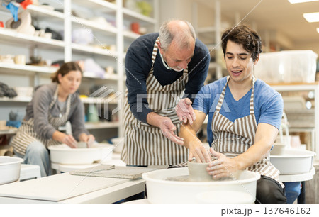 Eldery man helping young guy shape pottery on wheel 137646162