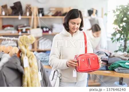 Woman looks at products in store and selects handbag. 137646240