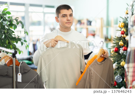 guy chooses cotton T shirts on the background of a Christmas tree 137646243