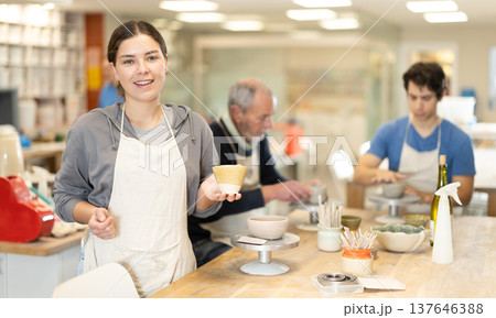 Smiling female potter demonstrates a clay cup he made with his own hands 137646388