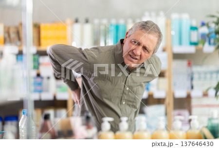 Older man experiencing sharp back pain while shopping in pharmacy Older man experiencing sharp back pain while shopping in pharmacy 137646430