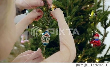 Father and daughter hanging delicate glass house ornament on pine branches, sharing festive christmas tree decorating moment with soft seasonal warmth Father and daughter hanging delicate glass house ornament on pine branches, sharing festive christmas tree decorating moment with soft seasonal warmth 137646501