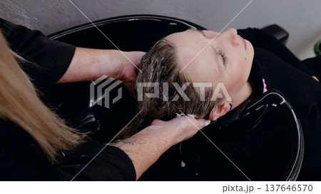 Hairdresser gently massaging and washing client's hair with shampoo in a salon sink, creating a relaxing and pampering experience 137646570