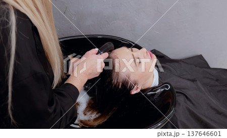 Hairdresser providing top notch hair washing service in a cozy salon with soothing water, shampoo, and treatment for a relaxing experience 137646601