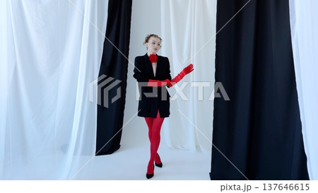 Fashion model wearing crimson gloves, sheer tights, black fitted blazer with scarlet floral pin, posing against monochrome studio backdrop for dramatic, high fashion look Fashion model wearing crimson gloves, sheer tights, black fitted blazer with scarlet floral pin, posing against monochrome studio backdrop for dramatic, high fashion look 137646615