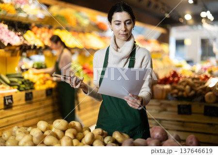 Young woman seller with phone takes inventory in vegetable shop Young woman seller with phone takes inventory in vegetable shop 137646619