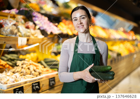 Female salesperson carefully places ripe cucumbers on counter of a grocery supermarket 137646628