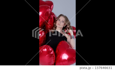 Glamorous woman posing confidently amid shiny red heart shaped balloons, radiating romantic elegance and celebratory mood Glamorous woman posing confidently amid shiny red heart shaped balloons, radiating romantic elegance and celebratory mood 137646631