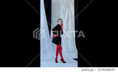 Stylish female model posing in vibrant red gloves, tights, black jacket, high heels against monochromatic curtain background, highlighting dramatic fashion contrast and textural elements Stylish female model posing in vibrant red gloves, tights, black jacket, high heels against monochromatic curtain background, highlighting dramatic fashion contrast and textural elements 137646643
