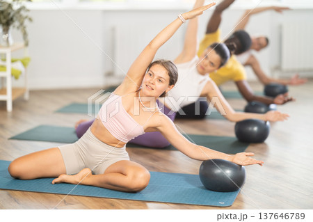 Young woman doing Mermaid Stretch with Ball in pilates class Young woman doing Mermaid Stretch with Ball in pilates class 137646789