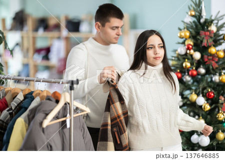 Girl tries on plaid jacket accompanied by guy in shop, X mas eve Girl tries on plaid jacket accompanied by guy in shop, X mas eve 137646885