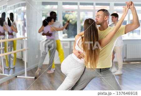 Happy young woman and man with group of international dancers training tango dance in dance class 137646918