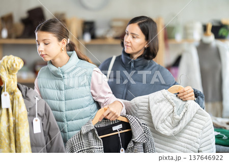 Mother and teen daughter looks at products in store and selects coat or jacket. Mother and teen daughter looks at products in store and selects coat or jacket. 137646922