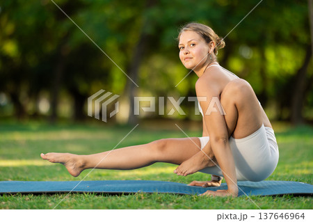 Girl in park on green grass of lawn performs Chakorasana 137646964