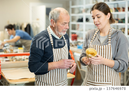 Young woman shows a clay cup she made to craftsman 137646978