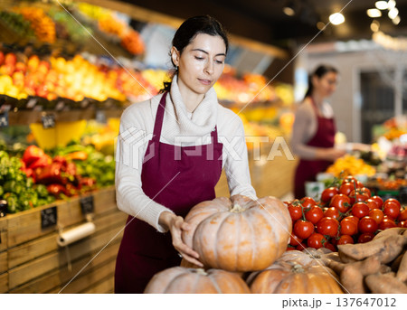 Woman seller offering pumpkins in a grocery store Woman seller offering pumpkins in a grocery store 137647012