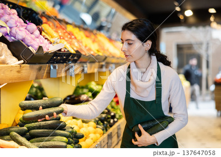 seller puts cucumbers on a shelf in a store seller puts cucumbers on a shelf in a store 137647058