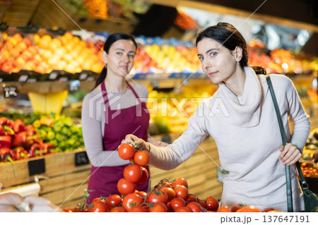 Woman shop assistant accompanies customer, help to choose tomato Woman shop assistant accompanies customer, help to choose tomato 137647191