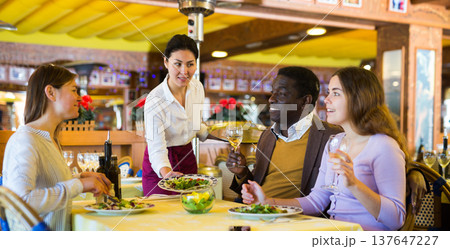 Asian waitress serving cheerful man and women over dinner in restaurant 137647227