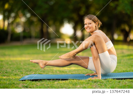 Sporty girl doing arm balancing Elephant Trunk Pose in summer park Sporty girl doing arm balancing Elephant Trunk Pose in summer park 137647248