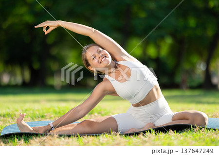Young woman practicing yoga on green glade in summer park 137647249