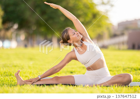 Girl in park on green grass of lawn performs Parivritta Janu Shirshasana Girl in park on green grass of lawn performs Parivritta Janu Shirshasana 137647512