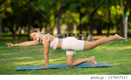 Girl in park on green grass of lawn performs Dandayama Bharmansana 137647521