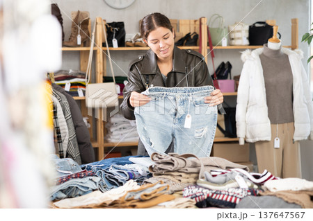 Girl chooses fashionable jeans trousers in clothing boutique Girl chooses fashionable jeans trousers in clothing boutique 137647567