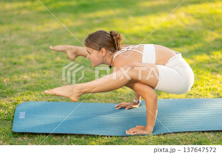 Girl in park on green grass of lawn performs Bhujapidasana Girl in park on green grass of lawn performs Bhujapidasana 137647572