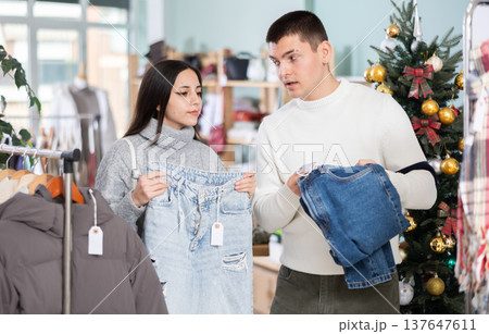 Married couple choose jeans against background of Christmas tree in clothing store Married couple choose jeans against background of Christmas tree in clothing store 137647611