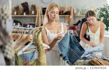 Woman holds shorts in her hands against the background of a customer in a store Woman holds shorts in her hands against the background of a customer in a store 137647630