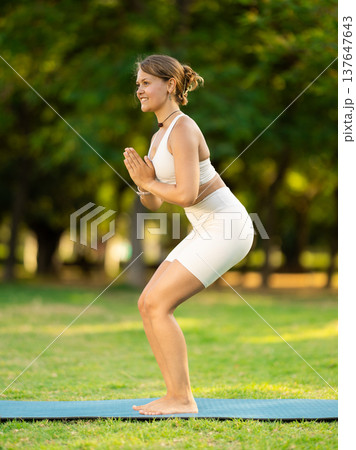 Girl in park on green grass of lawn performs utkatasana 137647643