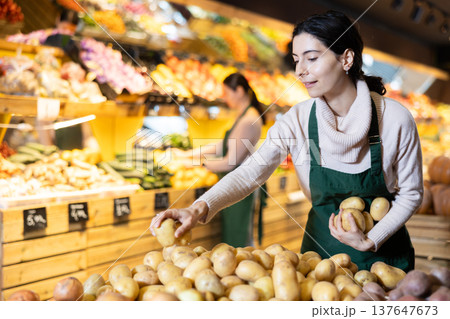 Young woman seller puts potatoes in vegetable shop 137647673