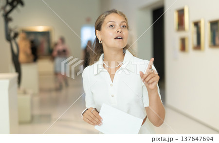 Portrait of young girl visitor with paper guide at the exhibition of paintings in museum 137647694