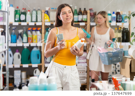 Woman consumer choose tanning product or sunscreen in household supermarket, while in background shoppers browse products 137647699