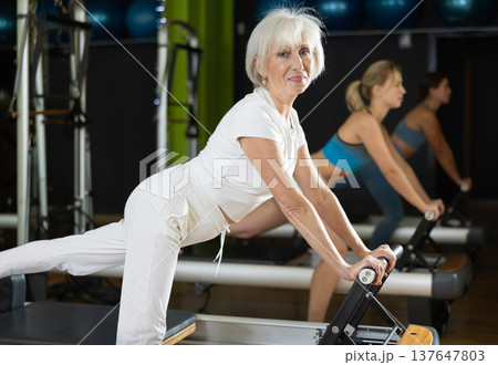 Senior woman standing on pilates reformer, perform exercises 137647803