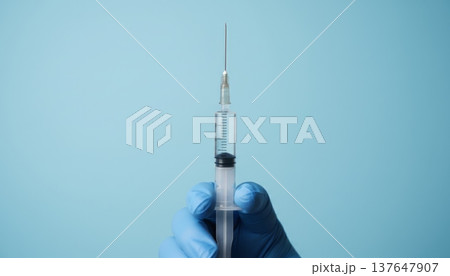Close Up of Blue Nitrile Gloved Hand Holding a Medical Syringe on Clean Blue Background Close Up of Blue Nitrile Gloved Hand Holding a Medical Syringe on Clean Blue Background 137647907