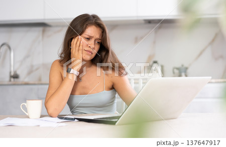 Young puzzled woman working on laptop in kitchen Young puzzled woman working on laptop in kitchen 137647917