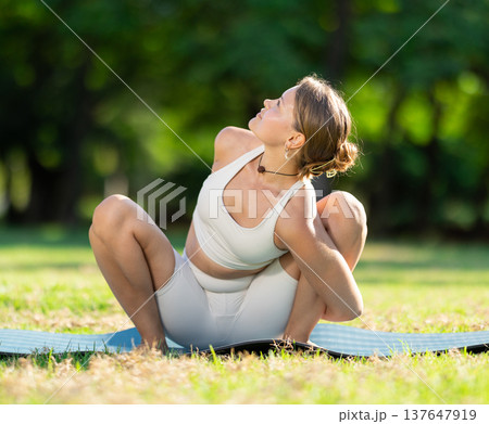 Girl in park on green grass of lawn performs Malasana Girl in park on green grass of lawn performs Malasana 137647919