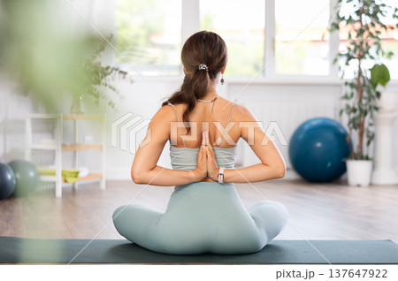 Young woman yoga trainer performing lotus pose variation on black rug Young woman yoga trainer performing lotus pose variation on black rug 137647922