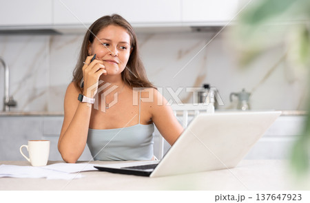 Young smiling woman working on laptop in kitchen Young smiling woman working on laptop in kitchen 137647923